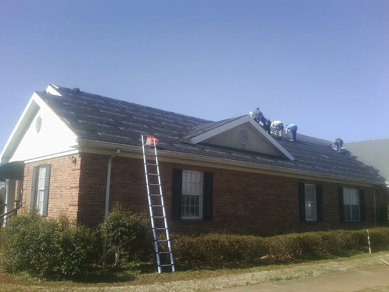 Crew tearing shingles off a brick ranch roof with a ladder set — Metal Roof Repair work by our crew in Deer Park