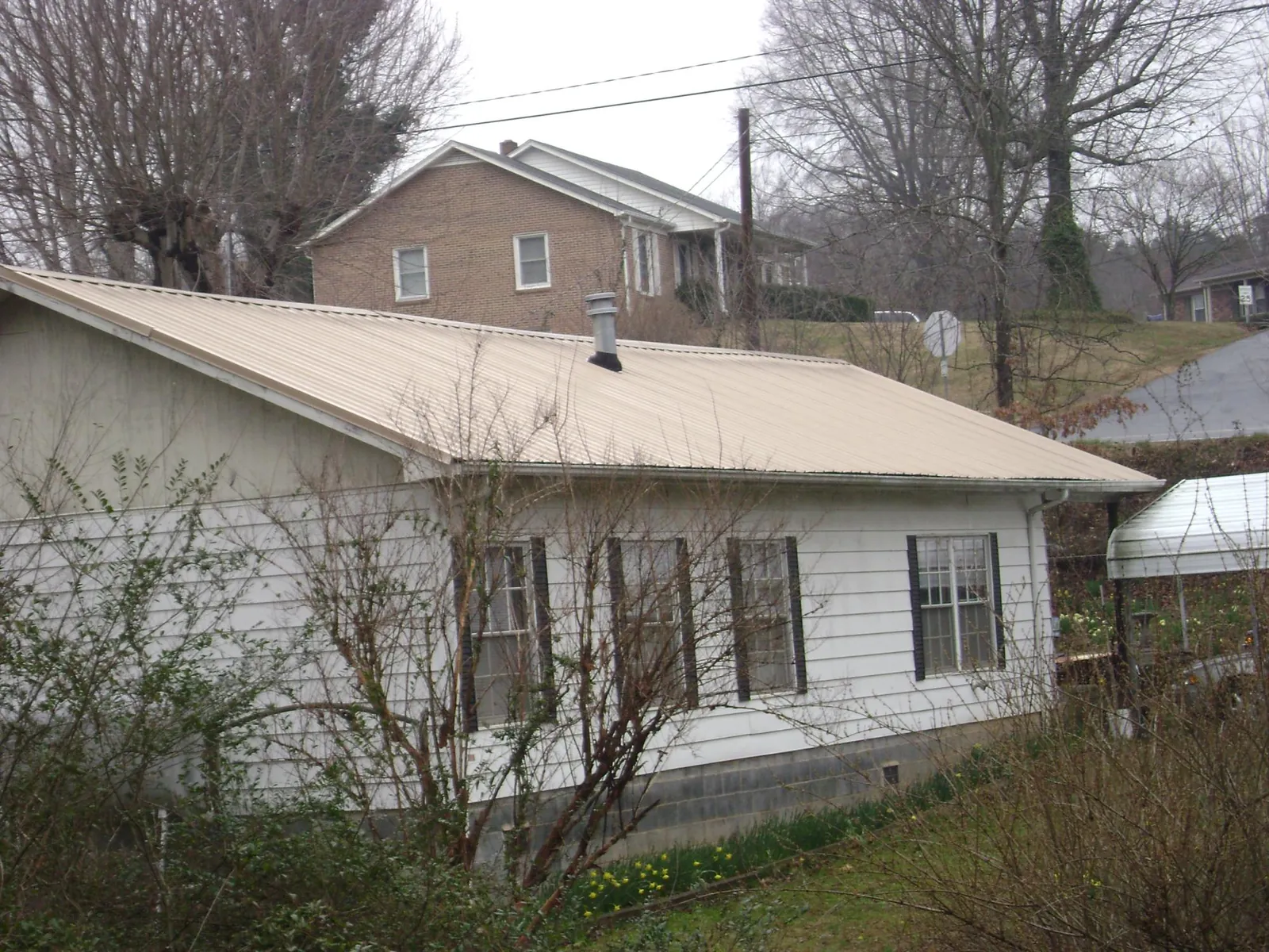 Tan metal roof on a white sided house set into a hillside — Commercial Roofing by Roofing Brothers in Deer Park
